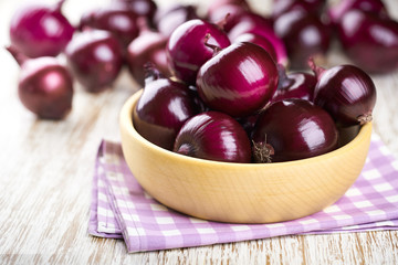 Red onions in wooden bowl on wooden table selective focus.