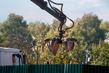 Grapple truck unloads scrap industrial metal for recycling. Manipulator with hydraulic magnet crab against sky.  Crane garbage truck loading industry waste. Crane grab scrap.