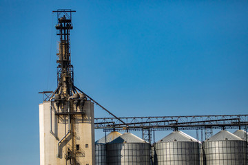Detail of a grain elevator connected to metal stockpile silos at an agrarian facility in Alberta, Canada. Against a blue sky with copy space above