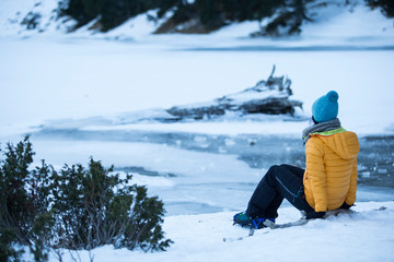 Fototapeta na wymiar Girl sitting on the shore of an icy mountain lake.