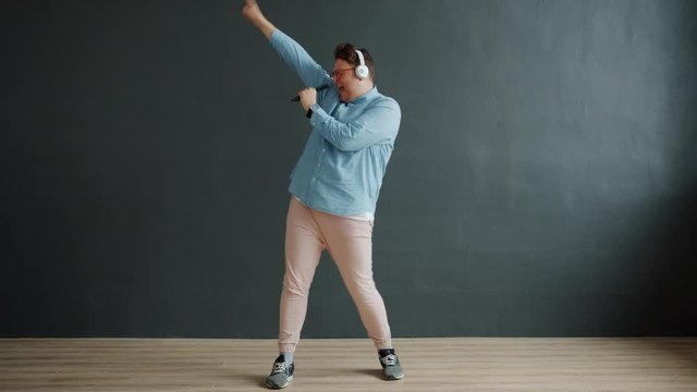 Funny stylish guy is singing dancing listening to music through headphones on dark background. Modern devices, happiness and entertainment concept.