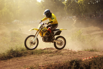 Motorcyclist in yellow uniform on dusty summer track in motocross competition