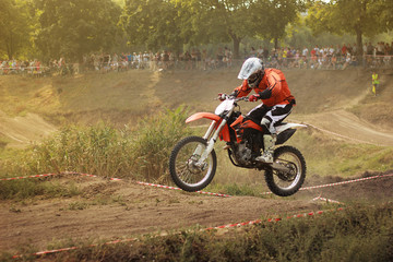 Motorcyclist in a jump at a motocross competition on a dusty summer track
