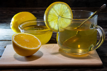 Tea with lemon in a glass, honey and a slice of lemon on the kitchen board.