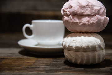 White marshmallows, in a white plate on a wooden table, against the background of white coffee cups.