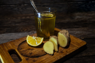 Tea with lemon in a glass, ginger root and a slice of lemon on the kitchen board.