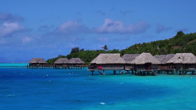 Low angle aerial glide view of overwater bungalow villas in turquoise lagoon. Bora Bora, Tahiti French Polynesia. Luxury honeymoon vacation, romantic getaway, exotic resort destination.  