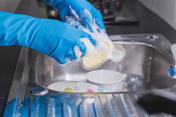 Close up of a man wearing a blue rubber glove was washing a spoon with a dish washing liquid in the sink in the kitchen.