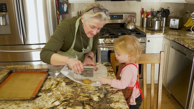 Kind and patient grandmother shows toddler how to make cookies while the baby steals and eats cookie dough