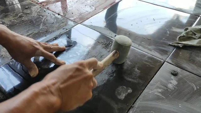 a male builder is installing black tiles in front of the house by hitting the black tiles with a bat so that the tiles can stick