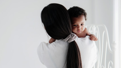 asian mother holding her black mixed race baby girl in white room