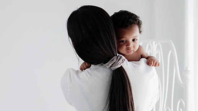 asian mother holding her black mixed race baby girl in white room