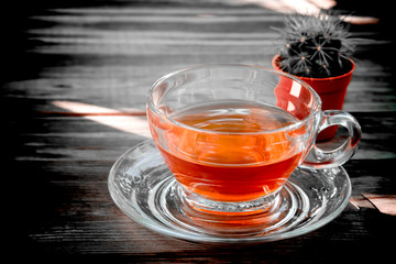 golden yellow amber tea in a clear colored teacup is placed on a dark wooden table and hard shadows background