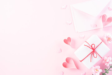 Pink paper hearts with cover letter and gift box on Light pink pastel paper background. Love and Valentine's day concept.