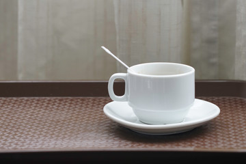 A white coffee cup with  plastic spoon inside over wooden background