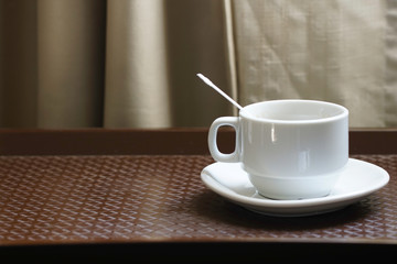 A white coffee cup with  plastic spoon inside over wooden background