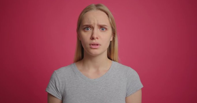 Upset crying blonde young girl at pink wall background slow motion