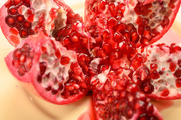 Ripe juicy pomegranate cut into several parts on a ceramic plate on a wooden background. Close up.