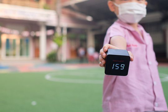 Little Asian Kindergarten Student Boy With Respirator Mask For Protection Holds PM2.5 Air Quality Monitor / Detector ,show Hazardous High Level Of Dust & Air Pollution At School Yard, PM 2.5 Concept