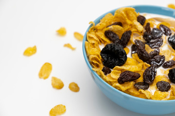 Cornflakes resin and dry prunes with fresh milk in the blue bowl on white background