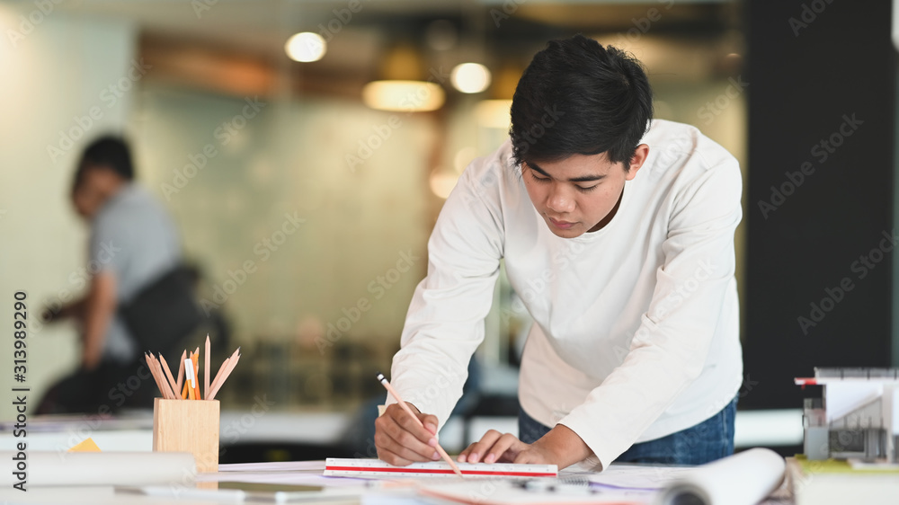 Poster front view photo of young architect man while he is drawing on the architecture plan at the working 