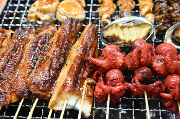 Different types of fish, octopusses and crabs on a grill in a market in Osaka-Japan.