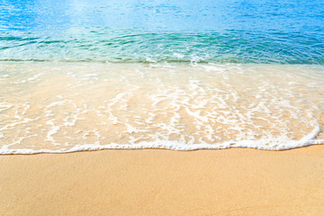Ocean wave on tropical beach with golden sand and ripple of water splash from emerald blue-green sea water during summer vacation.