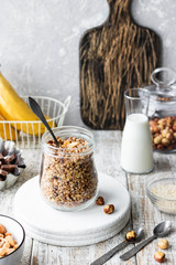 Chocolate banana granola with nuts in a glass jar on a light background