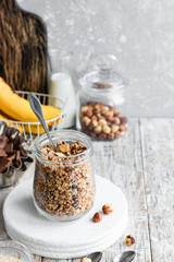 Chocolate banana granola with nuts in a glass jar on a light background