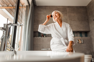 Cheerful old lady looking out of the window and combing hair