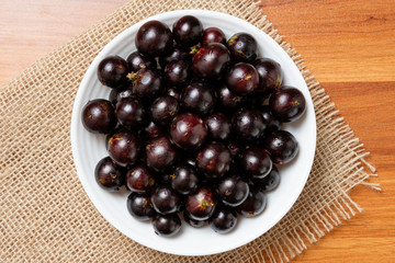 Jabuticaba in the bowl on wooden table - top view. Jaboticaba or Jabuticaba is the native Brazilian grape tree. Species Plinia Cauliflora. Brazilian Berry.