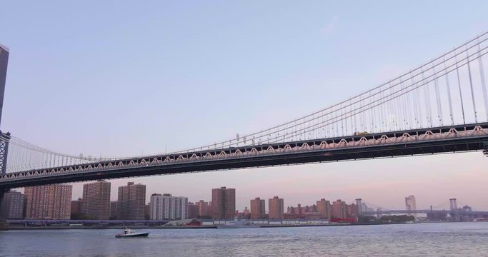 Slow pan of Brooklyn Bridge during sunrise with boats going across the Hudson River.