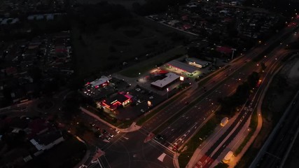 Aerial night shot of a busy service station next to a highway with cars driving by.