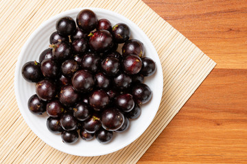 Jabuticaba in the bowl on wooden table - top view. Jaboticaba or Jabuticaba is the native Brazilian grape tree. Species Plinia Cauliflora. Brazilian Berry.