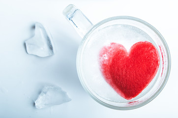 A mug with a frozen red heart inside and shards of ice on the table. The concept of unrequited love.
