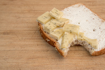Bite out of a slice of bread with cheese on wood cutting board. Healthy whole wheat bread with Gouda cheese with herbs and a creme cheese spread. 