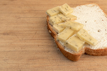 Slice of bread with cheese on wood cutting board. Healthy whole wheat bread with Gouda cheese with herbs and a creme cheese spread. 