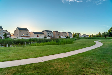 Grassy pond and pathway winding through lush green lawn with homes background