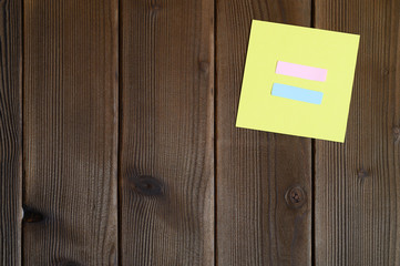 yellow sticky note with equal sign cut out of paper on a wooden background. space for text