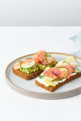 Smorrebrod - traditional Danish sandwiches. Black rye bread with salmon, cream cheese, cucumber, avocado on wooden background, vertical