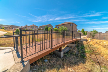 Side view of a bridge over a grassy terrain with homes and blue sky background