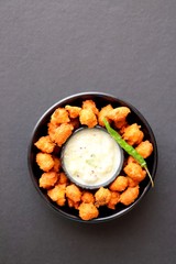 Moong and mix Dal Vada also known as ram laddoo, bhajias or fritters, served with fried chilli, curd & cucumber chutney or raita. Served over dark background. Selective focus. with copy space.