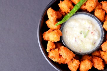 Moong and mix Dal Vada also known as ram laddoo, bhajias or fritters, served with fried chilli, curd & cucumber chutney or raita. Served over dark background. Selective focus. with copy space.