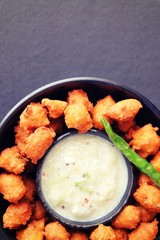 Moong and mix Dal Vada also known as ram laddoo, bhajias or fritters, served with fried chilli, curd & cucumber chutney or raita. Served over dark background. Selective focus. with copy space.
