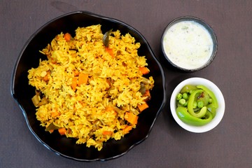ndian Vegetable Pulav or Biryani made using Rice and vegetables like peas, carrots, beans. served with raita and saute peas, capsicum bowl.