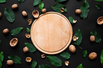 nutshell and fresh green leafs  scattered on a black background. Wooden cutting board in the centre