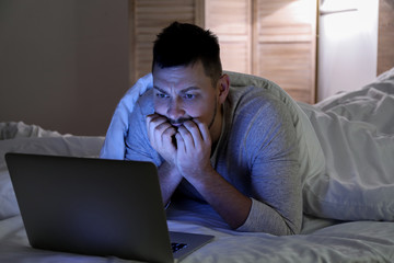 Emotional man with laptop in bed at night