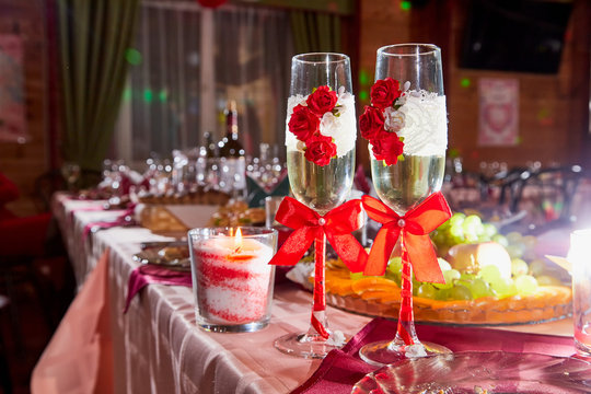 Two Glasses Decorated With Red Flowers And Bows On The Banquet Table