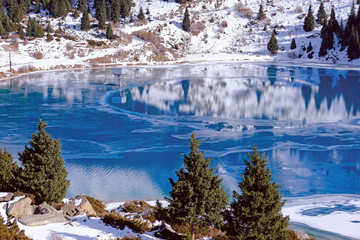 Autumn gives way to winter, air temperature drops and the water in the lake begins to freeze. Texture and patterns of ice on the serene water surface of a mountain lake; Big Almaty lake in Kazakhstan