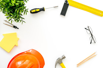 Construction concept. Helmet, tools on work desk, house cutout on white background top-down frame...